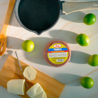 Fela Panela round panela on wooden board with cheese, lime, and skillet, a touch of authentic Latin flavor.