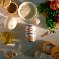 La Fe Pinto Beans can surrounded by fresh ingredients: garlic, onion, rice, tomatoes, and spices for authentic Latin meals.