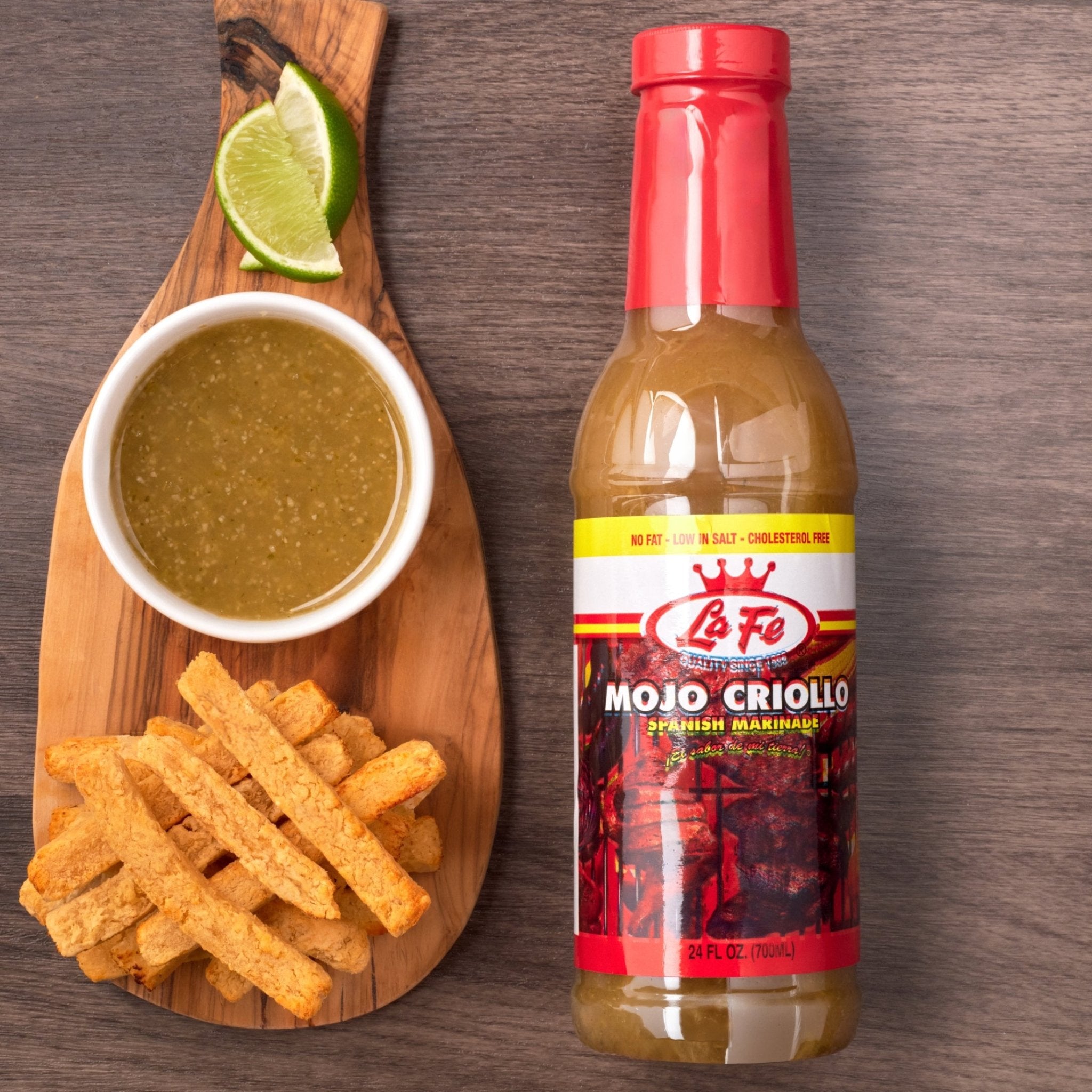 LA FE Mojo Criollo marinade with sauce, lime, and crispy plantains on a wooden board, ideal for Latin cuisine.