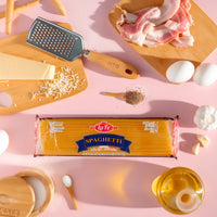 La Fe Pasta Spaghetti on a pink surface surrounded by kitchen ingredients, perfect for creating authentic Latin meals.
