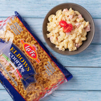 LA FE Elbow Pasta package next to a bowl of pasta salad topped with tomatoes, showcasing delicious Latin flavors.